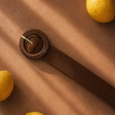 Cinto castanho com fivela circular e limões amarelos numa superfície castanha