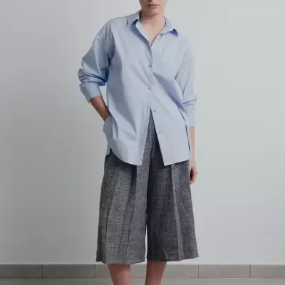 Mulher com camisa azul clara e calças culottes cinza xadrez.