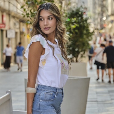 Mulher com t-shirt branca de mangas com padrão floral e jeans azul claro numa rua da cidade.