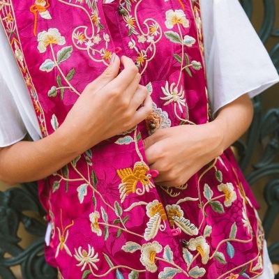 Colete rosa bordado com padrão floral colorido sobre camisa branca.