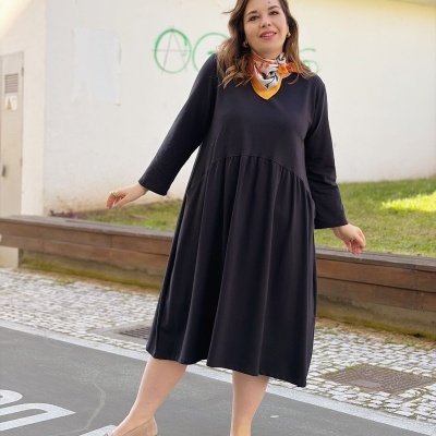 Mulher com vestido preto e lenço colorido, sapatos baixos bege, em rua e calçada