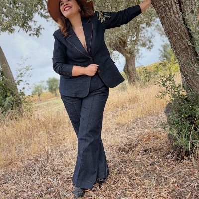 Mulher com conjunto de fato azul escuro e chapéu castanho em ambiente natural junto a árvores