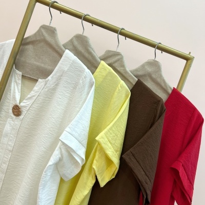 Camisolas de algodão branco, amarelo, castanho e vermelho penduradas num cabide de madeira