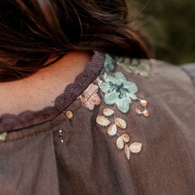 Detalhe de blusa com bordados florais e decote rendado castanho