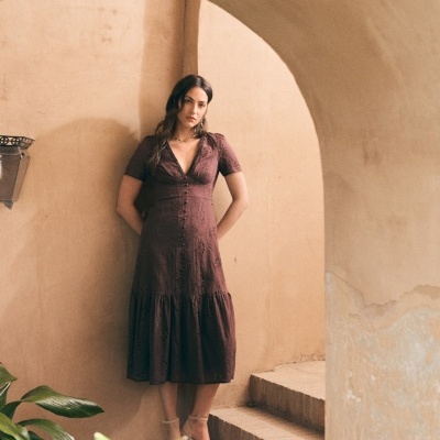 Mulher a usar vestido midi castanho com bordado e decote em V, em escadaria com plantas e paredes rústicas