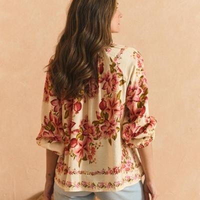 Blusa feminina flores rosa e verde fundo bege com calças jeans claras.