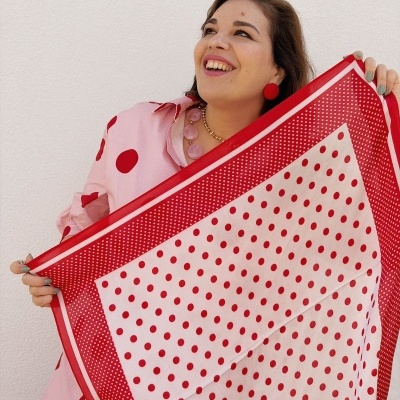 Mulher segurando lenço branco com bolinhas vermelhas, vestindo camisa rosa com bolinhas vermelhas