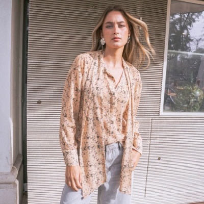 Mulher com blusa floral bege e calções de ganga cinza junto a parede metálica cinza com aviso de alta tensão