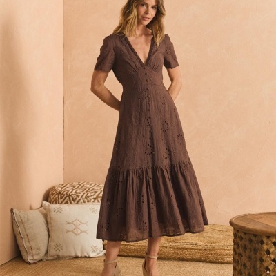 Vestido comprido castanho com bordados e botões usado por mulher em ambiente interior rústico