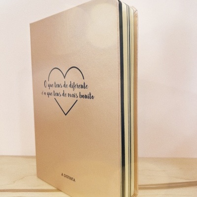 Caderno bege com frase inspiradora e coração preto na capa.