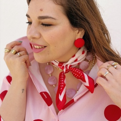 Mulher com blusa rosa de bolinhas vermelhas e acessórios em tons vermelhos e dourados