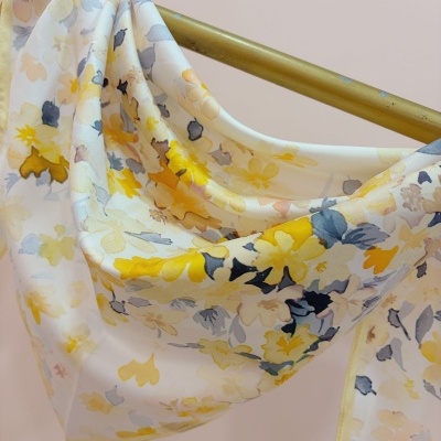 Lenço floral amarelo e cinzento pendurado num suporte dourado