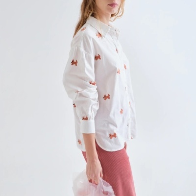 Camisa branca com estampado de cães laranja usada por mulher que segura sacos plásticos com copos.