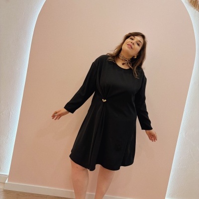 Vestido preto com mangas compridas e detalhe na cintura, sandálias castanhas e lenço ao pescoço em ambiente interior