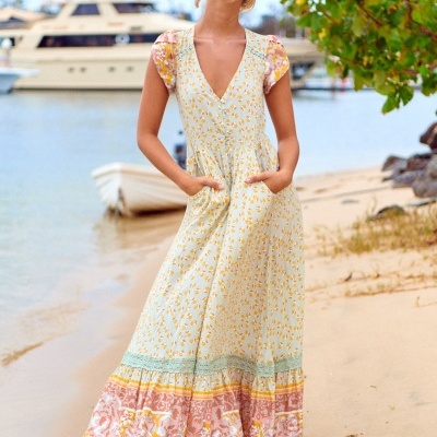 Vestido comprido com padrão floral amarelo e rosa numa praia
