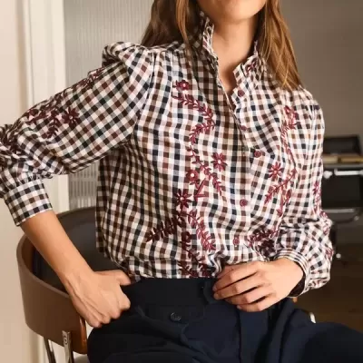 Camisa xadrez com bordados florais vermelhos e calças pretas numa cadeira