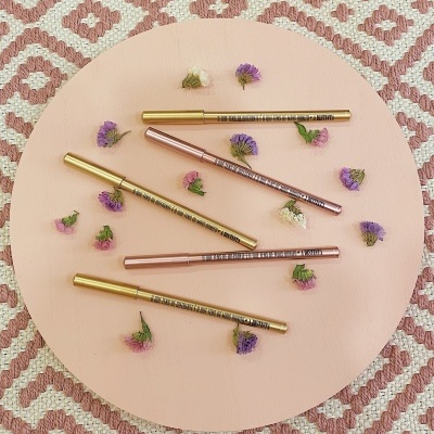 Set de canetas metálicas douradas e cor de rosa sobre fundo rosa claro e tapete rosa e branco com flores secas