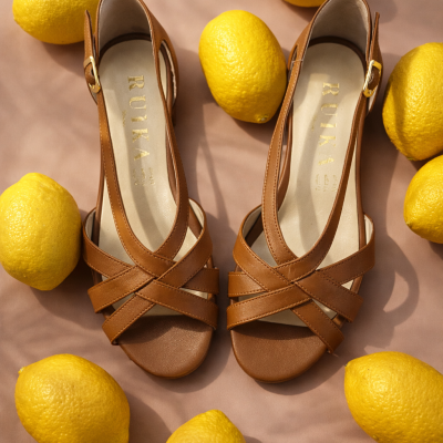 Sandálias castanhas de couro com tiras cruzadas e limões amarelos ao redor