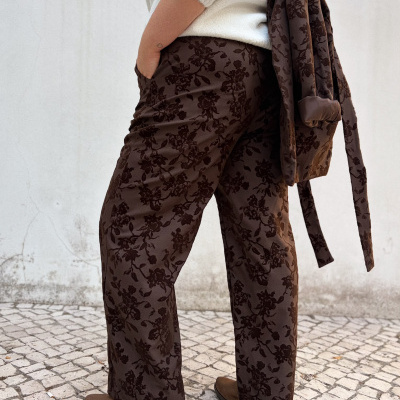 Calças e casaco castanhos com padrão floral, camisola creme, botas castanhas e pavimento em calçada portuguesa.