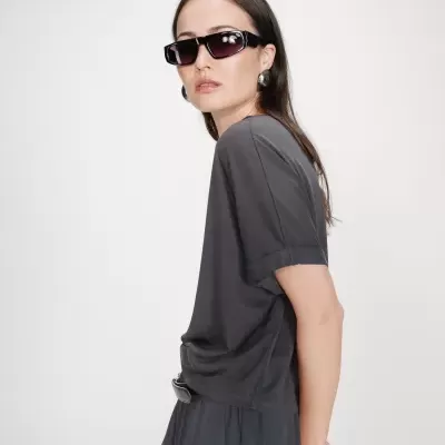 Mulher com óculos de sol pretos, brincos prateados e roupa cinzenta