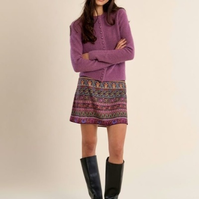 Mulher com camisola roxa, saia estampada e botas pretas