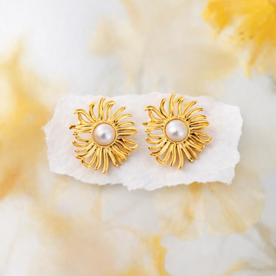 Brincos dourados com pérola branca no centro sobre papel branco