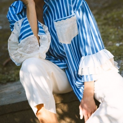 Blusa azul às riscas com renda branca e calças brancas em ambiente exterior.