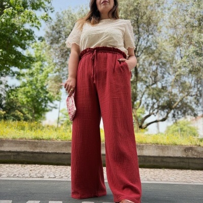 Mulher vestida com blusa bege, calças largas vermelhas e sandálias castanhas ao ar livre
