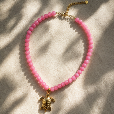 Colar com contas cor-de-rosa e pendente dourado sobre tecido bege