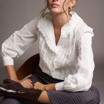 Mulher sentada com blusa branca rendada e calças xadrez cinzentas