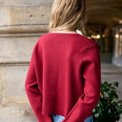 Mulher de costas com camisola vermelha e calças de ganga, segurando livro