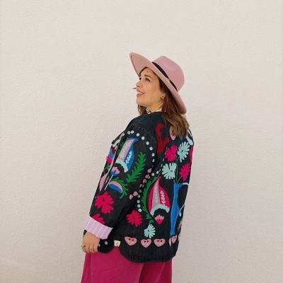 Mulher com casaco preto floral, calças rosa e chapéu rosa claro