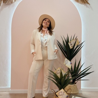 Mulher vestida com fato creme e chapéu bege em fundo arco cor-de-rosa com plantas e envelopes decorativos