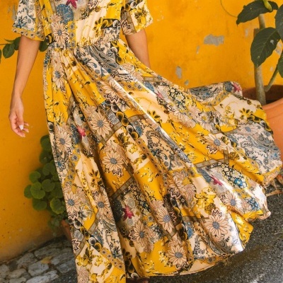 Vestido longo amarelo com estampa floral e padrão colorido junto a uma parede amarela.