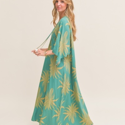 Vestido longo verde com padrão de folhas douradas usado por mulher em fundo neutro