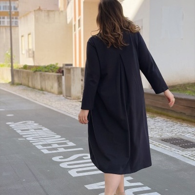 Pessoa de costas com vestido preto e sapatos beige a caminhar numa rua urbana.