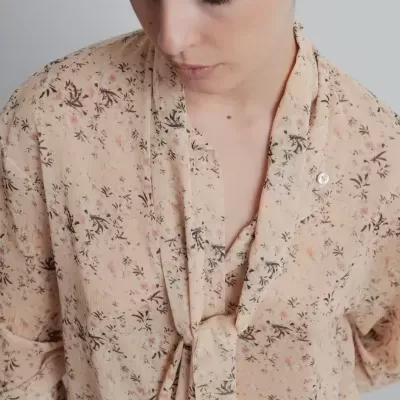 Blusa bege com padrão floral rosa e preto, gola amarrada, manga comprida