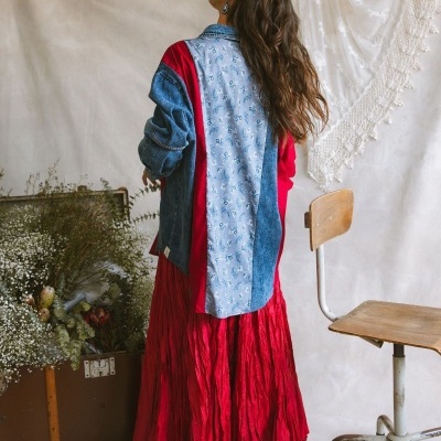 Casaco patchwork azul e vermelho, vestido vermelho comprido, cadeira antiga e flores secas em fundo claro.