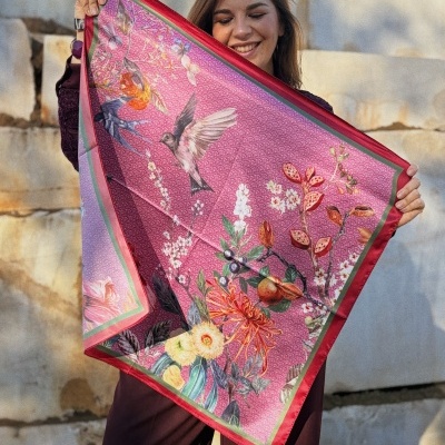 Lenço colorido com padrão floral e pássaros, segurado por mulher sorridente