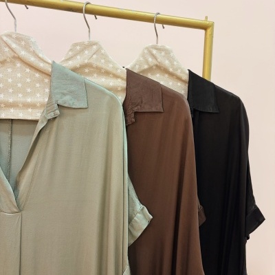 Três camisas de manga curta penduradas com capas bege com estrelas, em suporte dourado