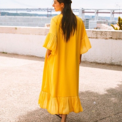 Vestido amarelo comprido com mangas e barra plissada usado por mulher ao ar livre