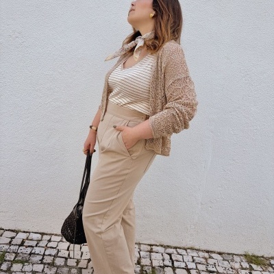 Mulher vestida com calças, camisola, cardigan, lenço ao pescoço, sandálias e bolsa