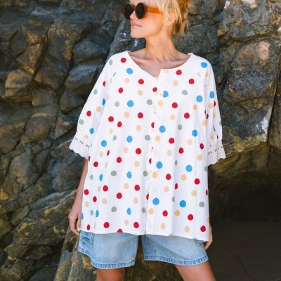 Blusa branca com bolinhas coloridas e calções de ganga em fundo rochoso