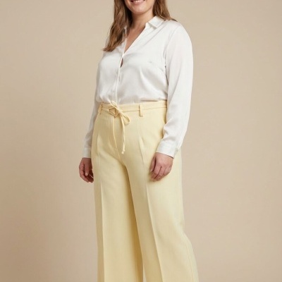 Mulher com camisa branca e calças amarelas largas num fundo bege