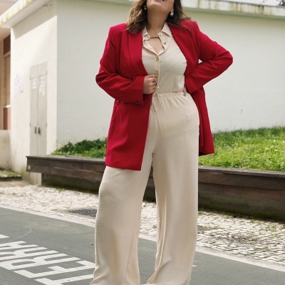 Mulher a sorrir vestindo blazer vermelho e calças largas creme na rua