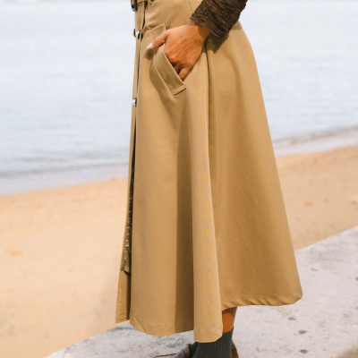 Saia midi beje com cinto e botões usados com camisa castanha e sapatos castanhos junto à praia