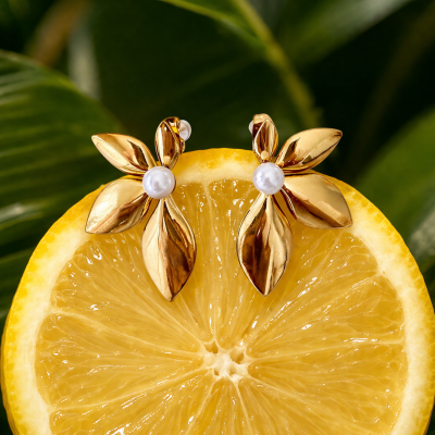 Brincos dourados em forma de folhas com pérolas, sobre fatia de limão e fundo de folhas verdes