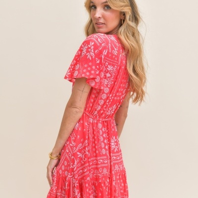 Vestido coral com padrão branco e mangas curtas com folho em fundo neutro.