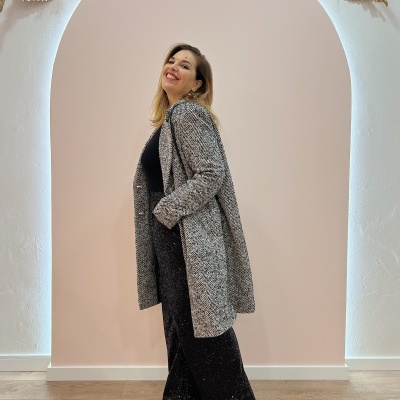 Mulher com casaco cinzento padrão espinha de peixe e calças pretas brilhantes