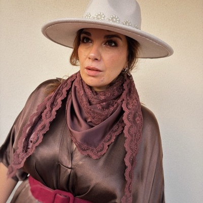 Mulher com chapéu bege adornado com flores bordadas e lenço bordô de renda